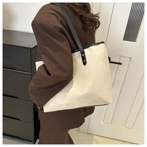 Chic cream tote bag with cracked leather texture and black straps on a female model