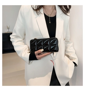 Détail d'une pochette en cuir verni matelassé noir avec fermeture dorée tenue par un mannequin