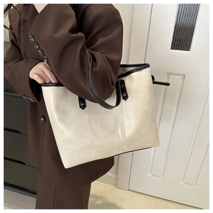 Detailed side view of cream white faux leather tote bag with black trim on a female model
