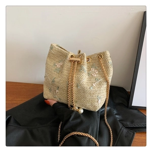 Detail of woven bucket bag featuring pink floral embroidery and pearl chain strap
