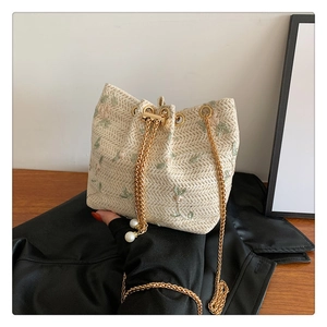 Detailed macro of beige straw bucket bag with floral embroidery and gold chain strap