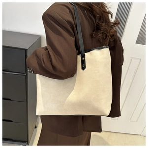 Detail of beige tote bag with textured faux leather, black straps and gold rivets