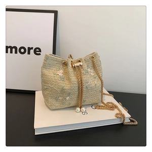 Detail of beige woven bucket bag featuring floral embroidery and pearl drawstring tassels