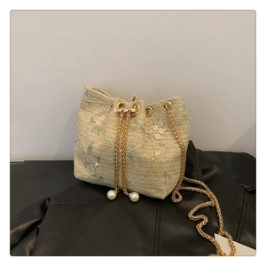 Detailed close-up of beige straw bucket bag with floral embroidery and pearl drawstring tassels