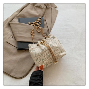 Detail of woven bucket bag with floral embroidery, chain strap and pearl drawstring