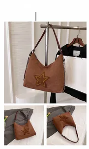 Detail of a brown suede hobo bag featuring a yellow star patch and metal chain strap