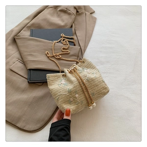 Detail of beige straw bucket bag with floral embroidery and elegant pearl drawstring accents
