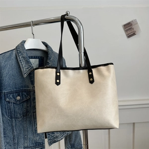 Minimalist beige tote bag with black shoulder straps and golden rivets on metal stand