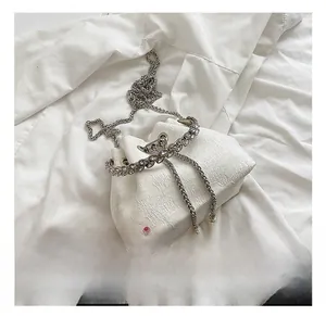 Detailed view of white bucket bag with sparkling rhinestone drawstring and pearl pendant