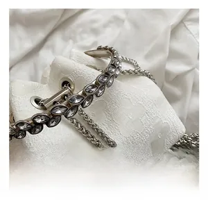 Close-up of a silver handbag handle with crystal inlay and chain detail with a pearl charm