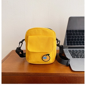 Detail view of the yellow canvas crossbody bag featuring a cute orange emblem and black strap