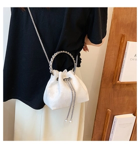 Detail of white drawstring bucket bag featuring floral texture, metal ring handle and pearl charm