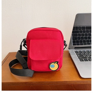 Close-up of red canvas crossbody bag with orange embroidery on a wooden desk