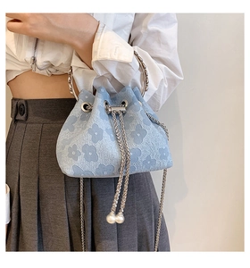 Detail of light blue bucket bag with floral texture, chain strap and pearl drawstring