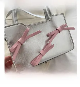 Détail du sac à main argenté métallisé avec trois nœuds en cuir rose et découpe stylisée unique