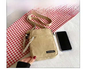 Detailed view of beige canvas crossbody bag next to a smartphone for size comparison