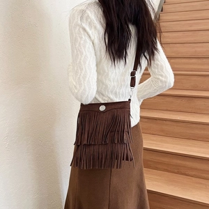 Detail of a dark brown suede bucket bag featuring layered tassels and a silver buckle accent