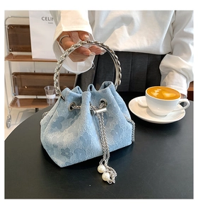 Close-up of light blue bucket bag with floral embossing, silver ring handle and pearl tassels