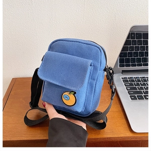 Detailed close-up of blue canvas crossbody bag featuring a bright orange patch embroidery