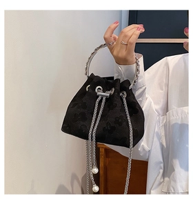 Detail of black drawstring bucket bag with floral texture, metal ring handle, and pearl charm