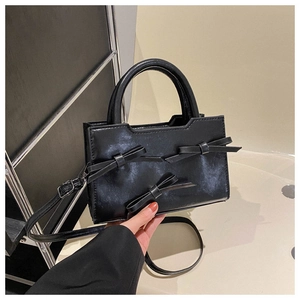 Détail d'un sac à main noir avec nœuds décoratifs et texture simili cuir brillant