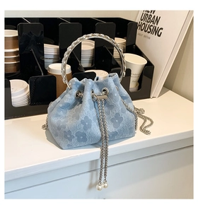 Detail of light blue bucket bag with floral jacquard texture and metallic ring handle