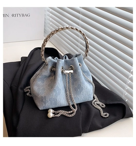 Detail of light blue bucket bag with floral embossing, metal ring handle and pearl drawstring