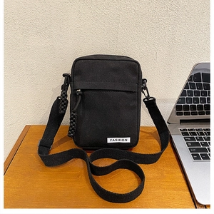 Detail of a black canvas crossbody phone bag featuring a zipper pocket and fashion label