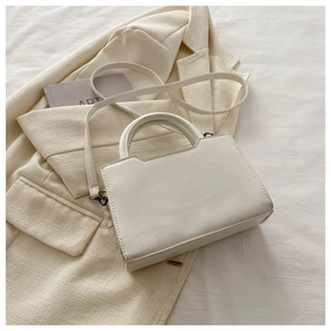 Détail du sac à bandoulière structuré blanc avec poignée à nœud sur fond en tissu