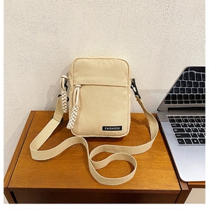 Close-up of beige canvas crossbody bag with Fashion label and woven zipper detail