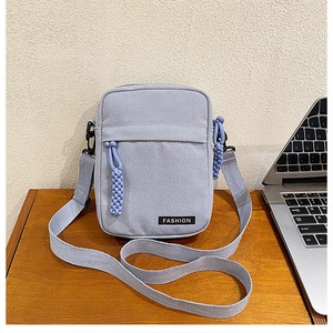 Close-up of a grey-blue canvas crossbody bag on a wooden desk with fashion label detail