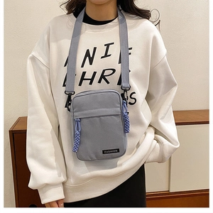 Detail view of a gray-blue canvas crossbody bag with dual zippers and a fashion label