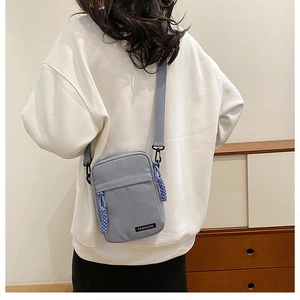 Close-up of light blue canvas crossbody bag with fashion label and woven zipper pull