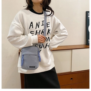 Detail of light blue canvas crossbody phone bag with fashion label and adjustable strap