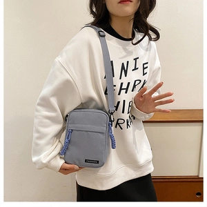 Detail of grey-blue canvas crossbody bag with purple zipper pull and fashion tag