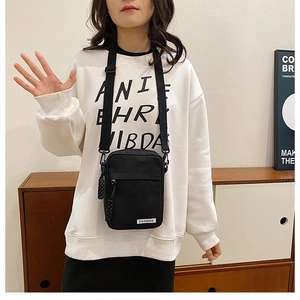Detailed shot of a black minimalist canvas crossbody bag with white FASHION label and woven puller