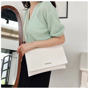 Close-up of a white envelope clutch bag with gold bar accent and metal chain strap