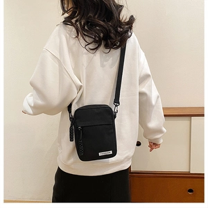 Detail of black canvas crossbody phone bag featuring fashion label and metal buckle