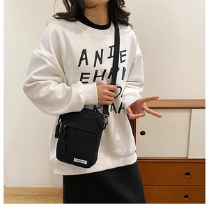 Detail view of black canvas crossbody bag featuring fashion label and braided zipper pull