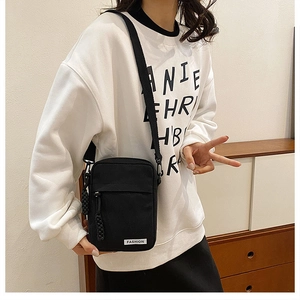 Close-up of black canvas crossbody bag with adjustable strap and white fashion label detail