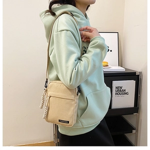 Detail of minimalist beige canvas crossbody bag showing fashion label and rope zipper pulls