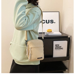 Detail view of beige canvas crossbody bag featuring fashion label and woven shoulder strap