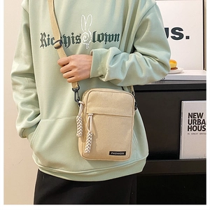 Detail view of beige canvas crossbody bag with adjustable strap and fashion label detail