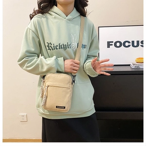 Close-up of beige canvas crossbody bag with adjustable strap and fashion logo label