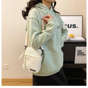 Close-up of cream canvas crossbody phone bag featuring a black fashion label and wide strap