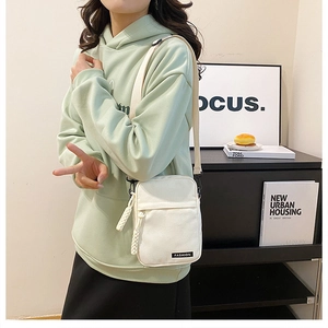 Detail showing an off-white canvas crossbody bag with adjustable strap and fashion label