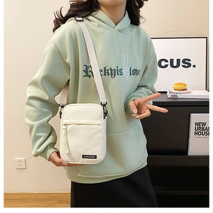 Detailed view of a white canvas crossbody bag with adjustable strap and front zipper