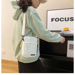 Close-up of a white canvas crossbody bag with adjustable wide strap and fashion label