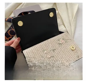 Détail du sac en paille tressée montrant les doubles boucles dorées et la broderie florale