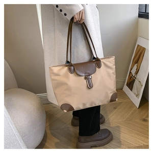 Detail of khaki nylon tote bag with brown leather trim and top handles in a lifestyle setting